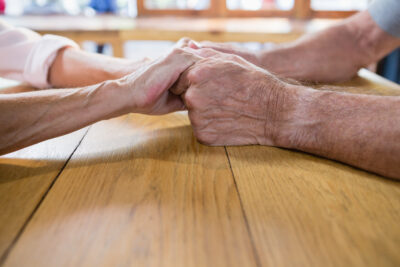 Older adult's hands resting on a table at home